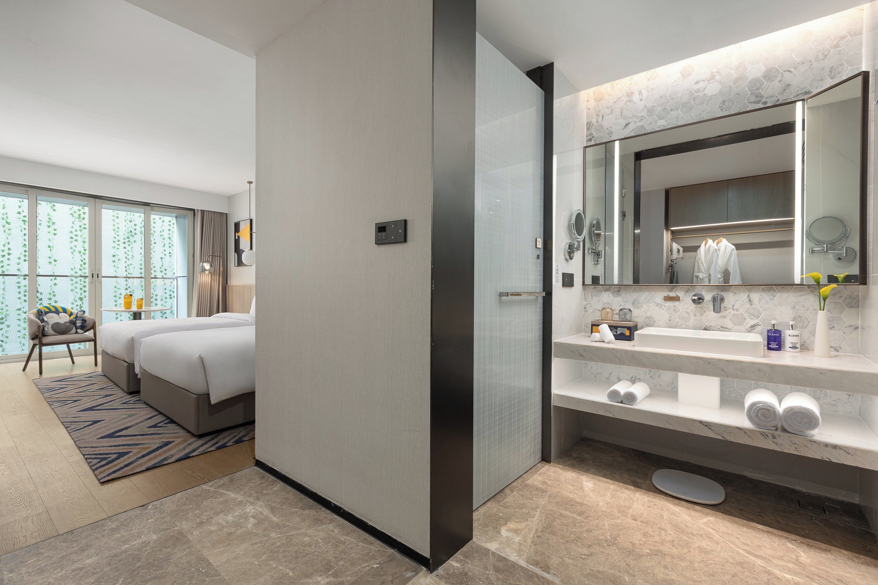 Ein modernes Hotelzimmer mit einem großen Bett, einem eigenen Badezimmer mit Waschtisch und Blick auf Grün durch das Fenster.