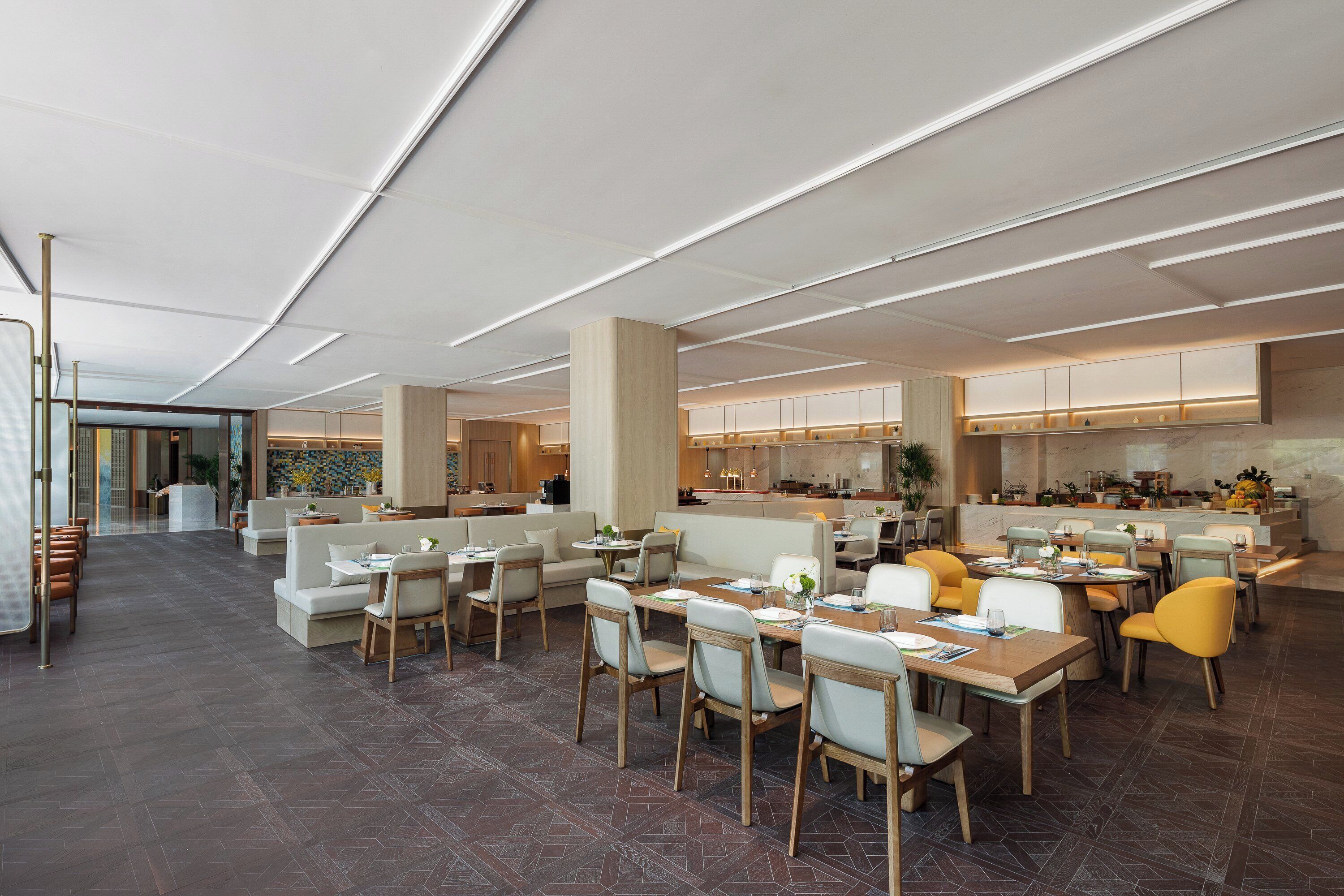 Een ruim restaurant met hoge plafonds, moderne verlichting en diverse zithoeken, waaronder tafels en banken.