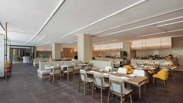 Een ruim restaurant met hoge plafonds, moderne verlichting en diverse zithoeken, waaronder tafels en banken.