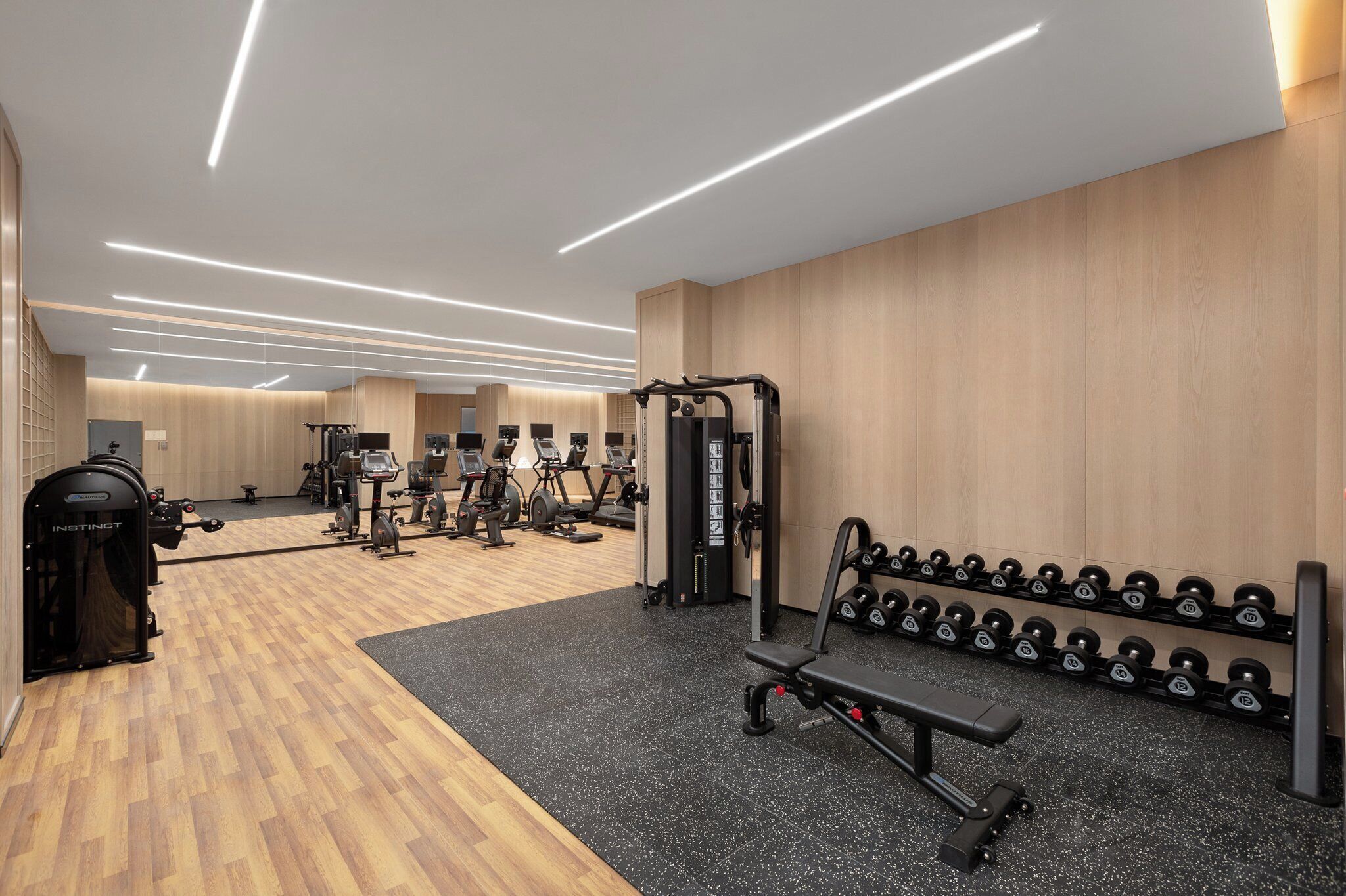 A modern gym with wooden flooring, exercise equipment, and a wall-mounted dumbbell rack.