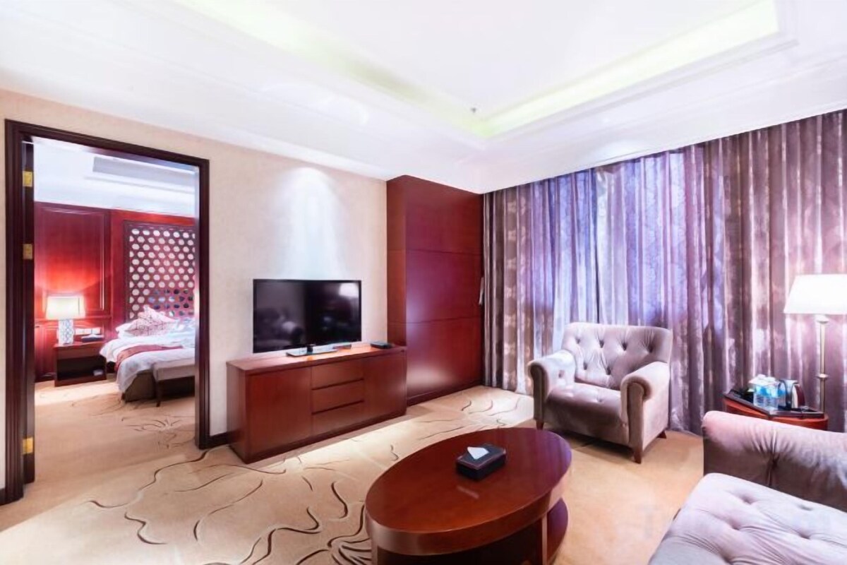 A hotel room with a bed, television, seating area, and curtains.