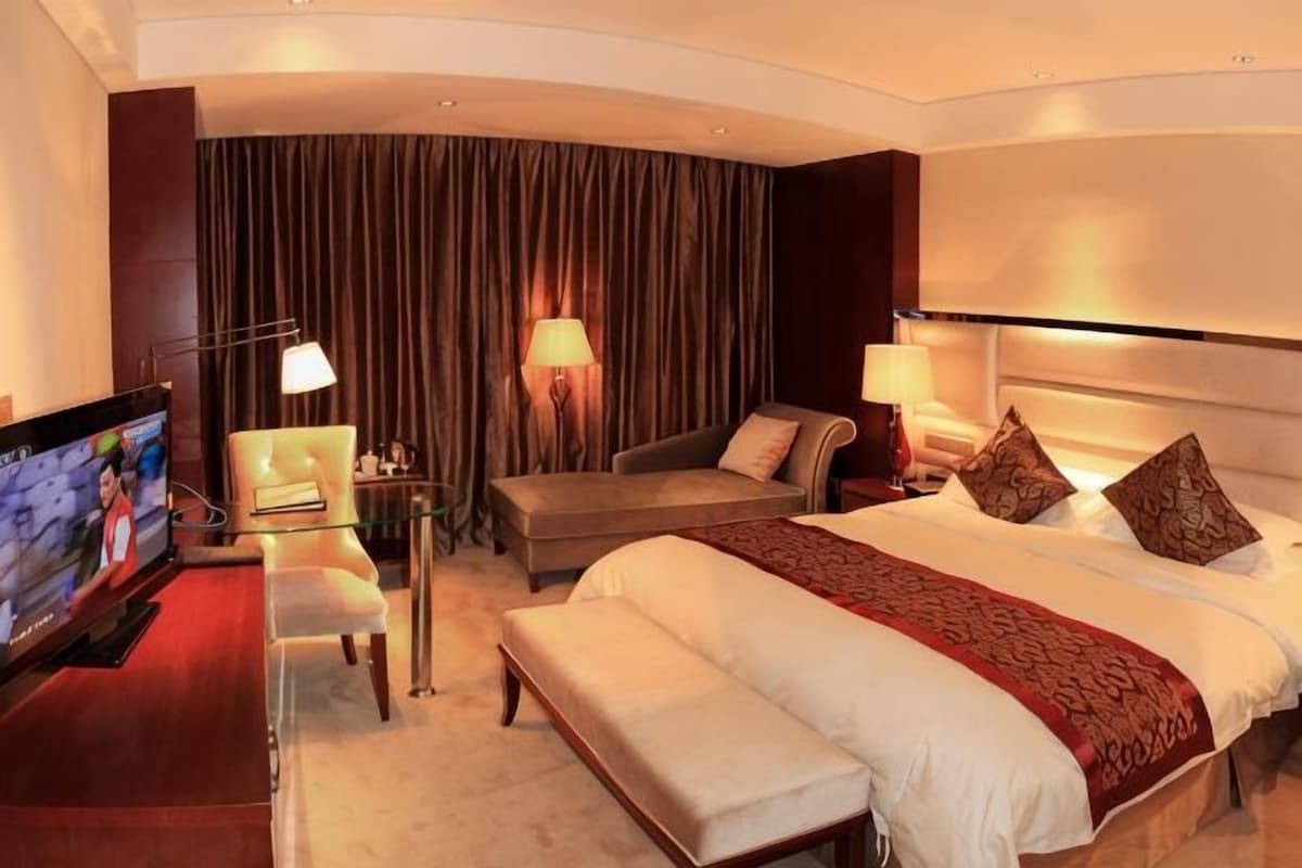 A hotel room with a large bed, a sofa, a TV, and a desk.