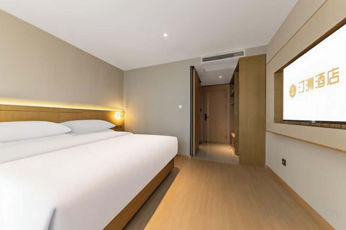 Een hotelkamer met een bed, nachtkastje, een aan de muur bevestigde televisie en een deur naar een andere kamer.
