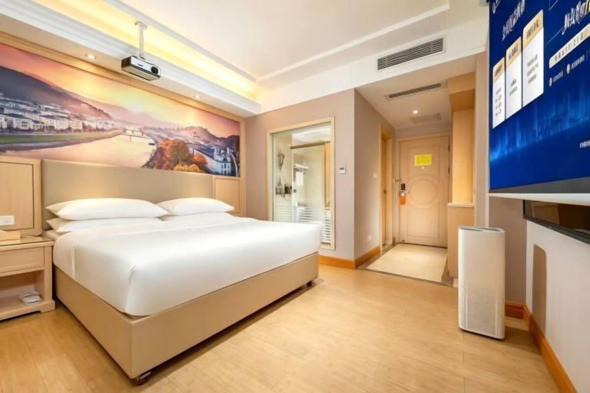 A hotel room with a large bed, a nightstand, a wall-mounted TV, and a painting above the bed.