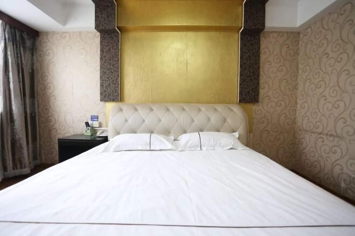 A neatly made bed with a tufted headboard, a bedside table with a lamp, and patterned wallpaper.