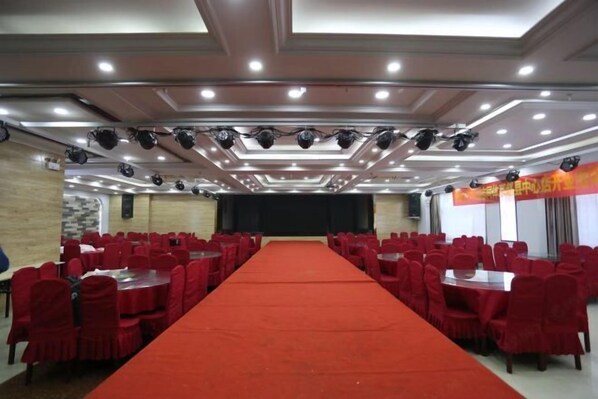 A conference room with a long red carpet, rows of red chairs, and a stage with a black backdrop. - Zhaoxian Friendship Hotel (Zhao County)