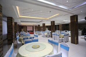 Un amplio salón de banquetes con mesas y sillas redondas, paneles de madera en las paredes y una pantalla de proyector al fondo.