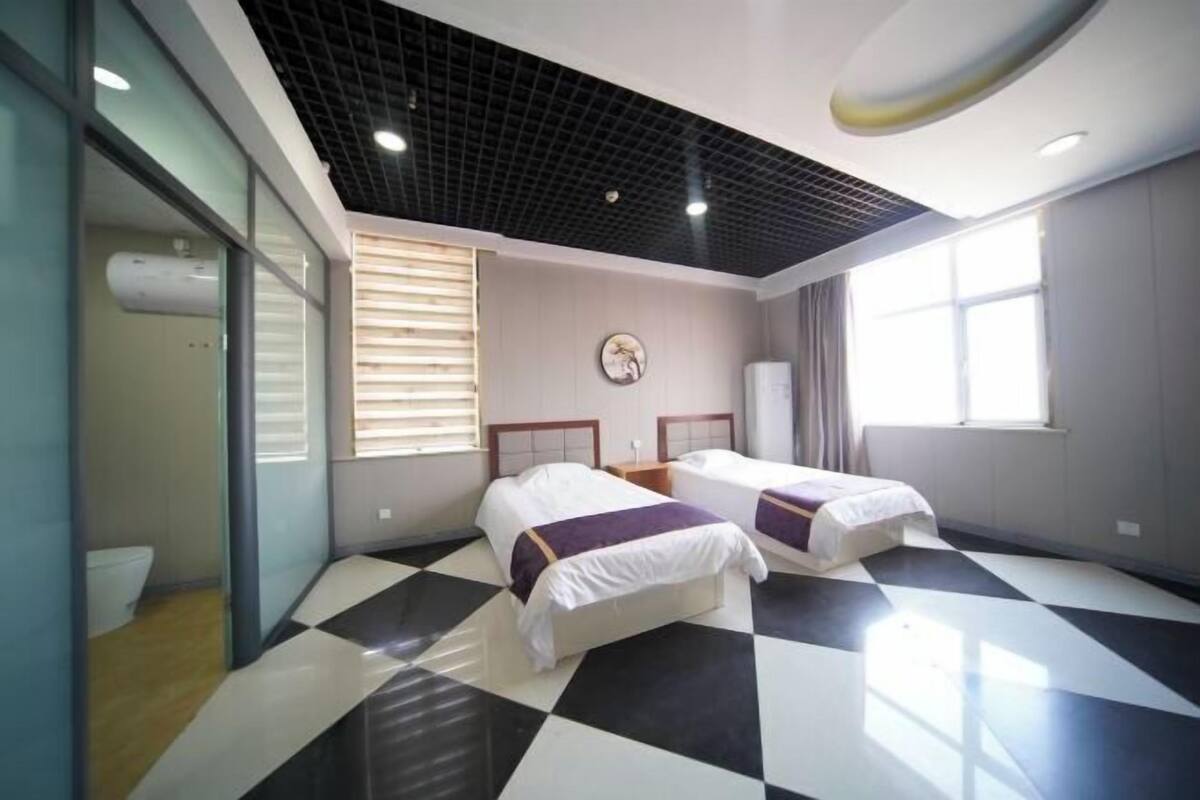 A hotel room with two beds, a black and white checkered floor, a large window, and a ceiling with a grid pattern.