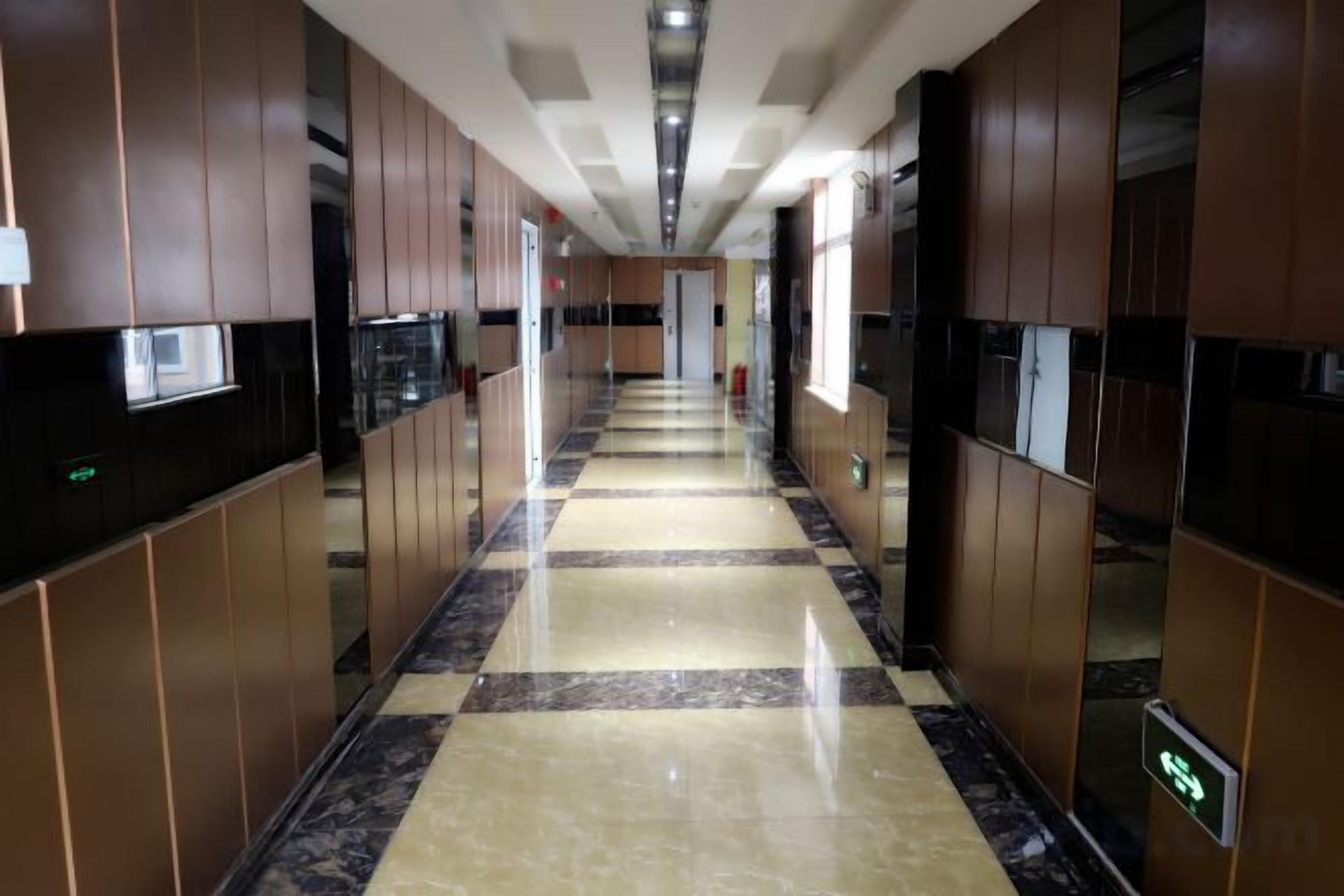 A hotel corridor with a checkered floor, mirrored walls, and a central elevator.