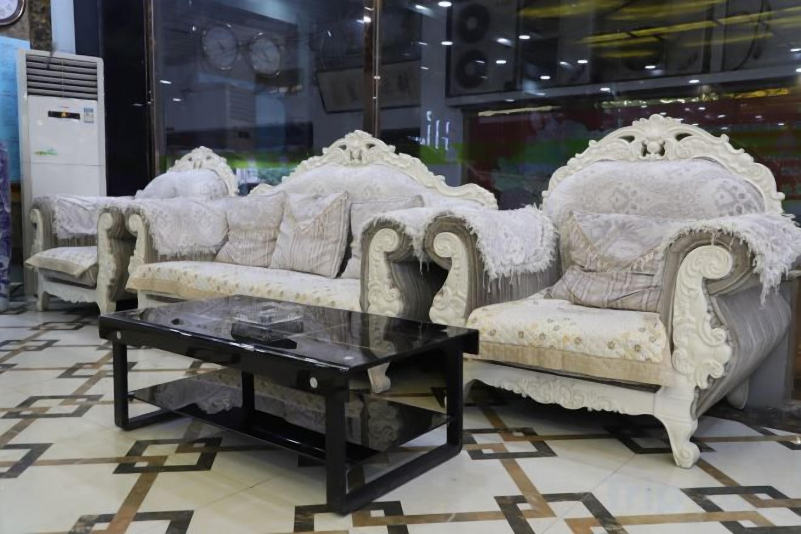 Un ensemble de canapés blancs à motifs, agrémenté d’une table basse en verre, dans une pièce dont le sol est recouvert d’un revêtement à motifs.