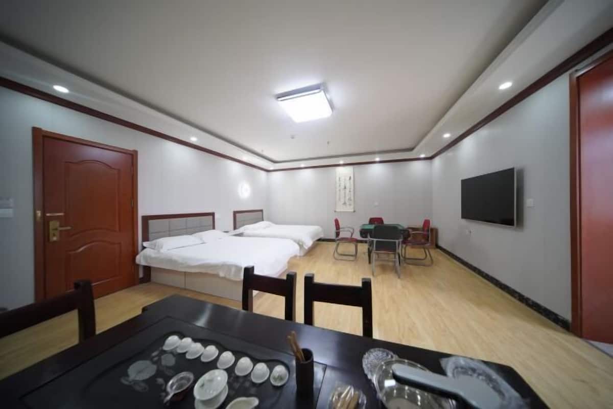 A hotel room with a bed, a desk, a chair, a TV, and a dining table with plates and cups.