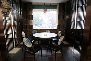 Un comedor con una mesa redonda y cuatro sillas, una ventana con vista a la calle y un adorno colgante.
