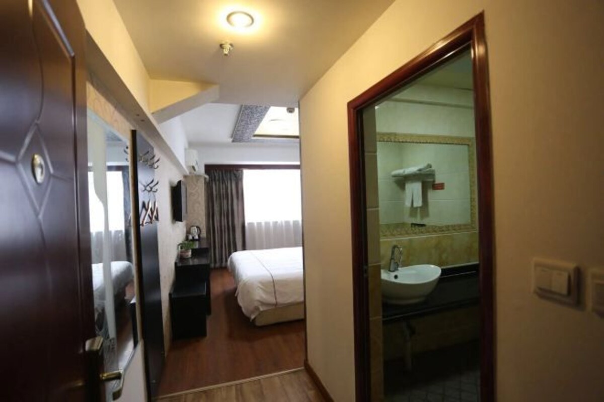 Quarto de hotel com cama, escrivaninha, espelho e banheiro com pia e espelho.