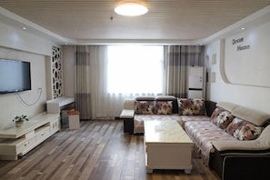 Una sala de estar moderna con un televisor de pantalla plana, un sofá, una mesa de centro y un ventanal con cortinas.