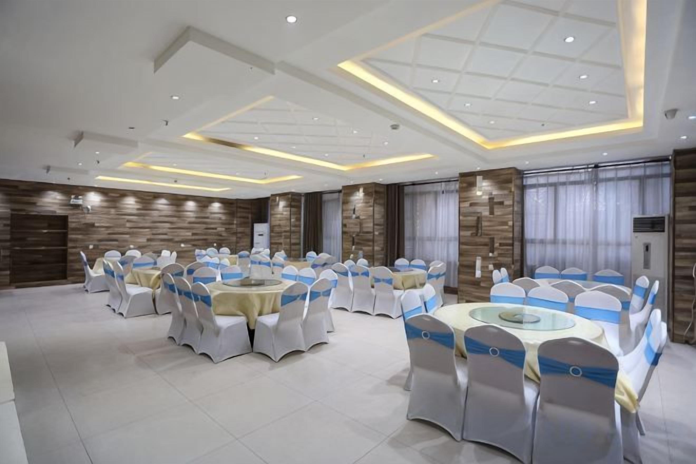 A banquet hall with round tables and chairs, recessed lighting, and a modern ceiling design.