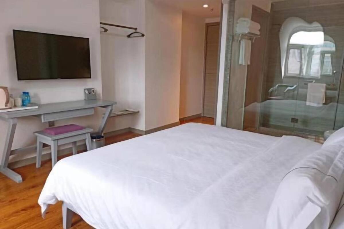 A hotel room with a bed, a desk with a chair, a television, and a glass shower enclosure.