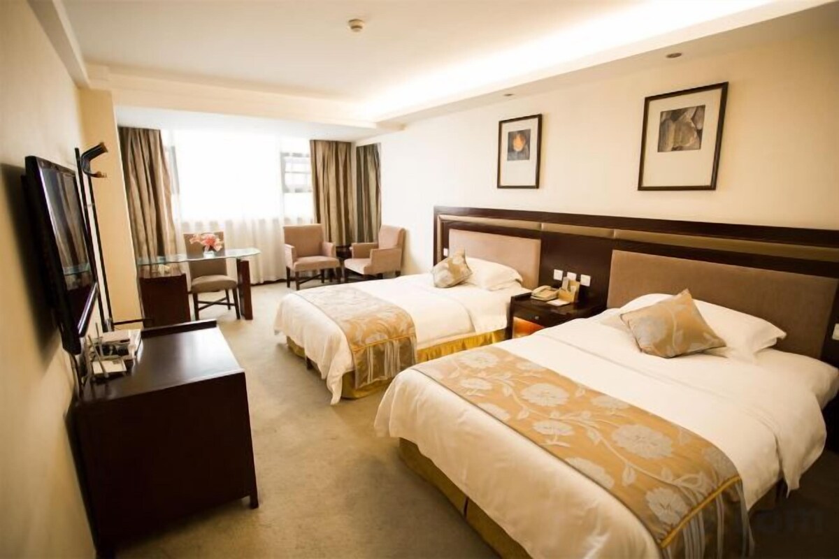 A hotel room with two beds, a desk, a chair, a television, and a window with curtains.