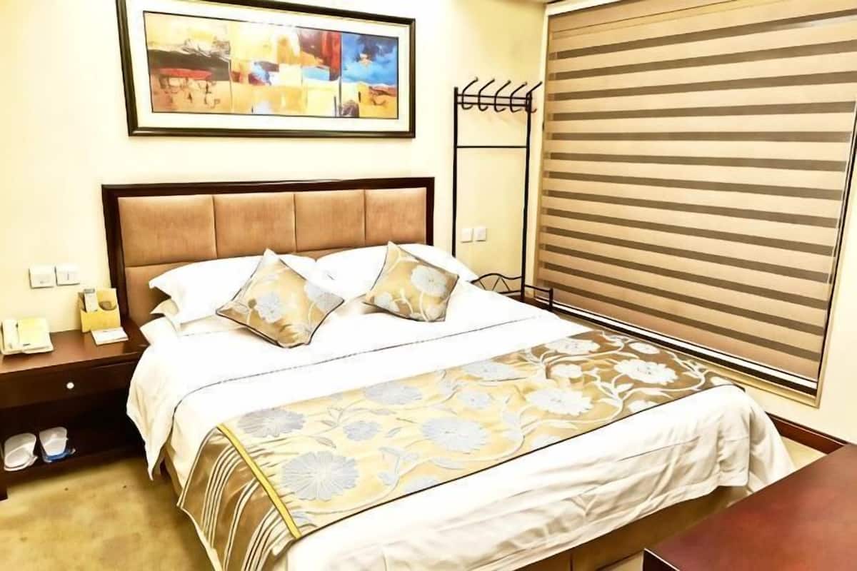 A hotel room with a bed, a nightstand, a telephone, and a window with blinds.