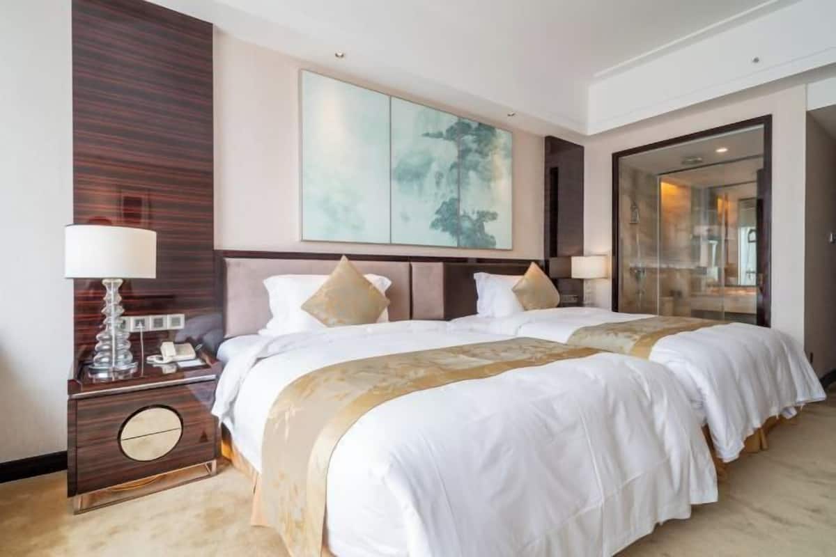 A hotel room with two beds, a large abstract painting, a nightstand with a lamp, and a mirror.