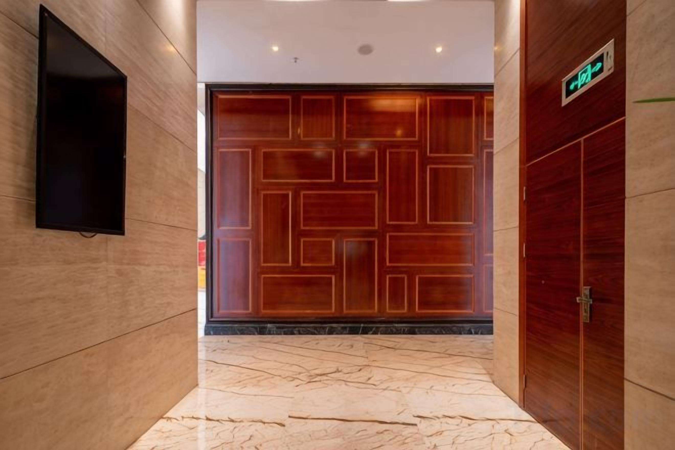 Un couloir avec une porte en bois, un téléviseur à écran plat fixé au mur et un sol en marbre.