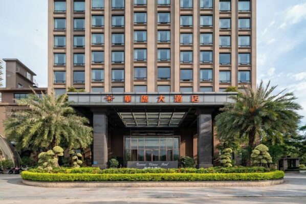 Un hotel de varios pisos con fachada moderna, un acceso cubierto y un jardín delantero arbolado.