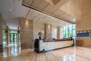 Un área de recepción con piso de mármol, un mostrador de recepción y un ventanal que proporciona luz natural.