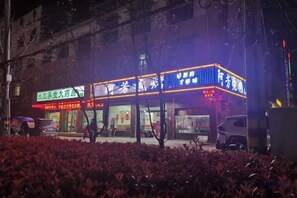 A brightly lit building with signage, a parking area, and a pathway leading to the entrance.
