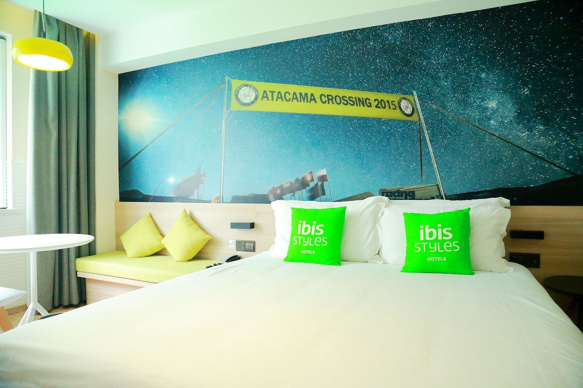 Ein Hotelzimmer mit Bett, Nachttisch, Lampe und Wandgemälde.