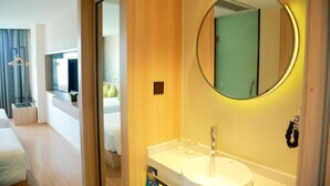 A modern hotel room with a wooden floor, a white bed, a round mirror with a light, a white sink, and a small window with curtains. - Ibis Styles Shanghai Qingpu Sports Center Hotel (Shanghai)