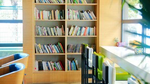 A bookshelf filled with books, a wooden desk, and chairs in a room with large windows. - Ibis Styles Shanghai Qingpu Sports Center Hotel (Shanghai)