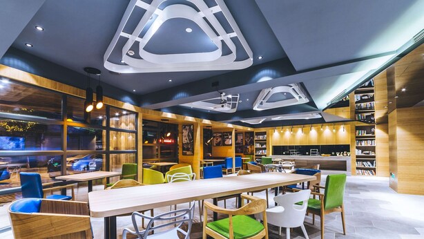 A modern restaurant with a variety of seating options, including tables and chairs, and a large bookshelf filled with books. - Ibis Styles Shanghai Qingpu Sports Center Hotel (Shanghai)