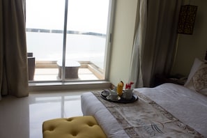 A hotel room with a bed, a window with curtains, a tray with breakfast items, and a yellow ottoman. - Sayeman Beach Resort (Cox's Bazar)