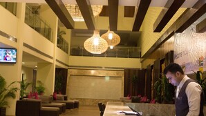 Een hotel lobby met een receptiebalie, een zithoek en een groot scherm waarop een sportevenement wordt vertoond.