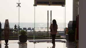 Een vrouw staat bij een glazen deur met uitzicht op de zee.