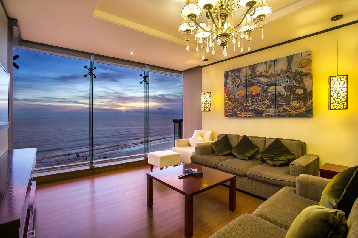 A modern living room with a large window, a chandelier, and a painting on the wall.