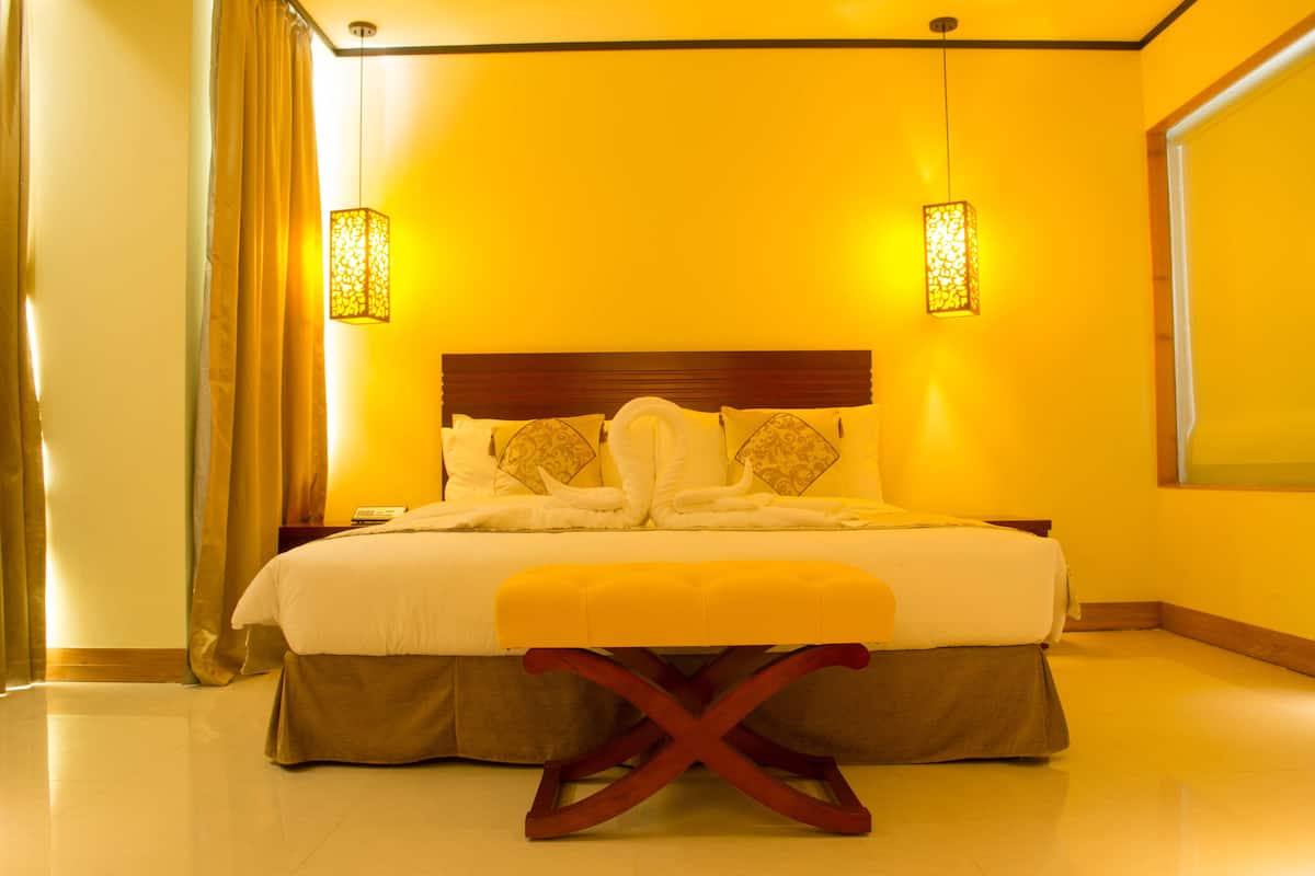 A hotel room with a large bed, a wooden headboard, two bedside lamps, and a bench at the foot of the bed.
