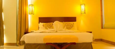 A hotel room with a large bed, a wooden headboard, two bedside lamps, and a bench at the foot of the bed.