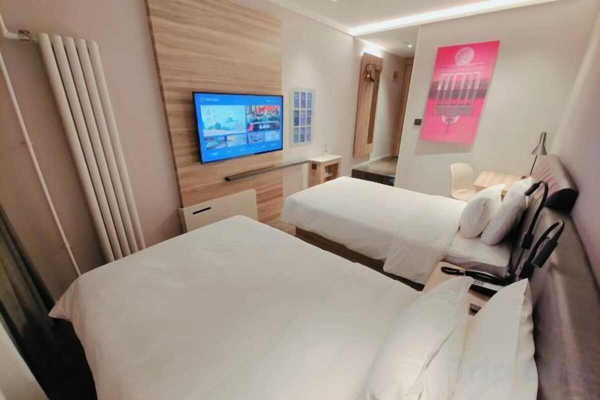 A hotel room with two beds, a TV, a mirror, and a poster on the wall.