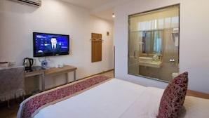 Una habitación de hotel con una cama, televisor, escritorio, espejo y ventana.