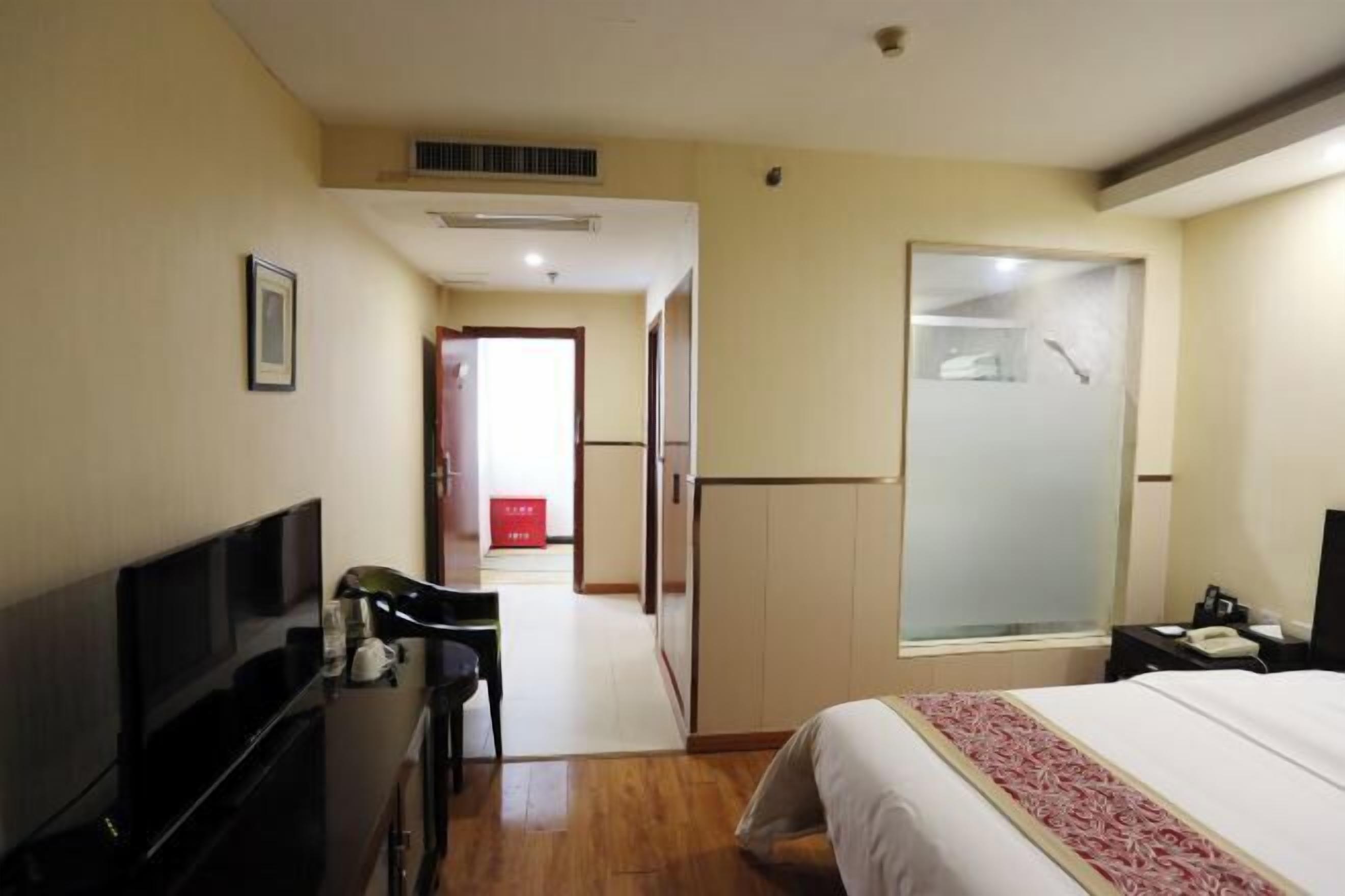 A hotel room with a bed, a TV, a desk with a chair, a wardrobe, and a bathroom with a mirror.
