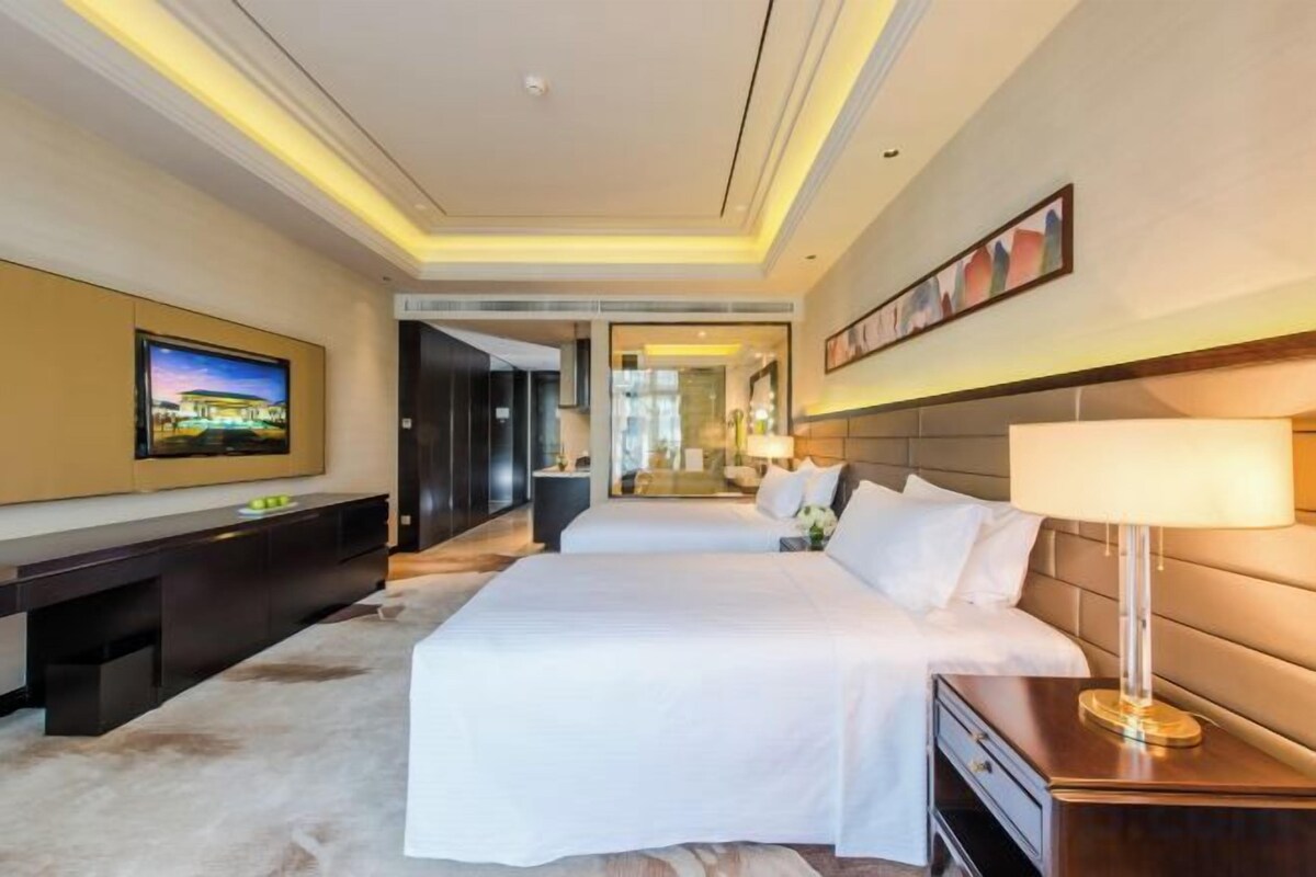 A hotel room with a large bed, a TV, a desk, and a lamp.