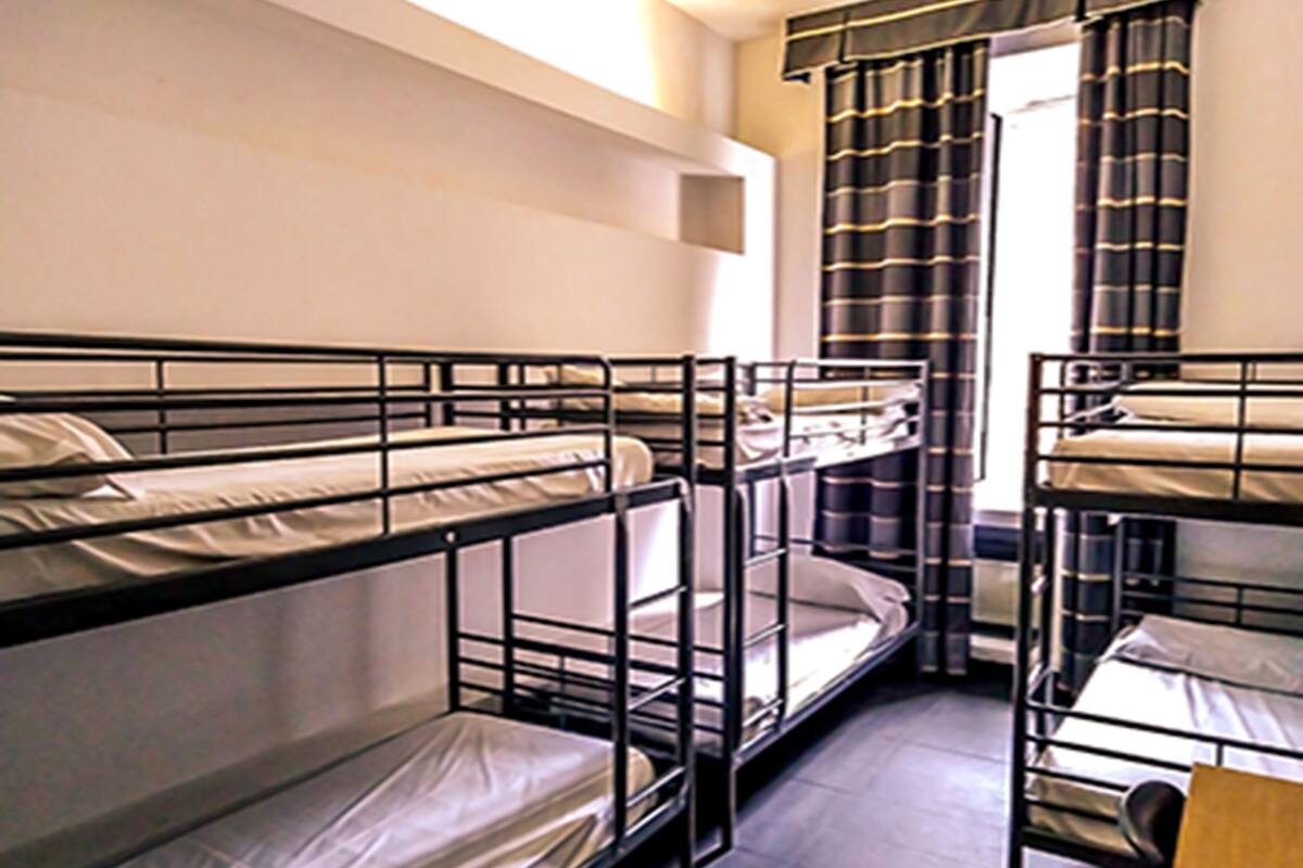 A dormitory room with bunk beds, a window with curtains, and a small shelf.