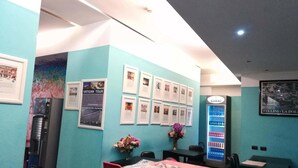 Un espace d’accueil avec un mur bleu, des tableaux encadrés, un distributeur automatique et une table avec un journal.