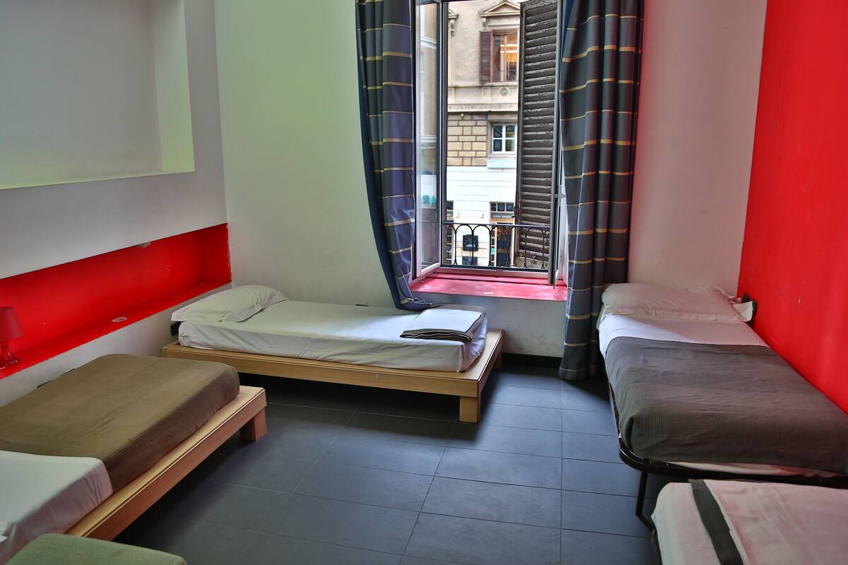 A room with two single beds, a window with curtains, and a red wall.
