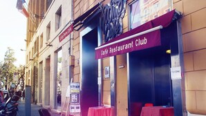 Un bâtiment avec une enseigne indiquant qu’il abrite un café-restaurant-club, des places assises en plein air et un panneau signalant une zone Wi-Fi.