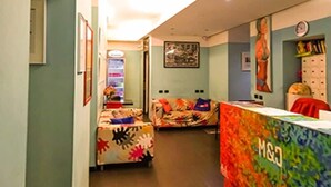 Un hall d’hôtel comprenant un comptoir d’accueil, un petit coin salon avec une table et des chaises, et un couloir menant à une autre pièce.