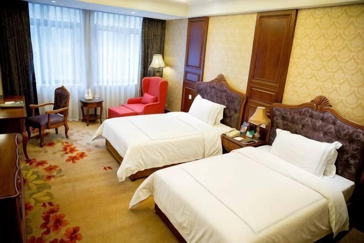 Habitación de hotel con dos camas, un escritorio, una silla y una lámpara.
