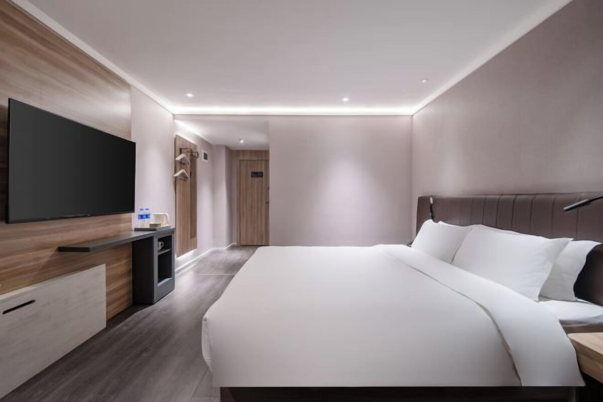 Una camera d'albergo moderna con un letto grande, una televisione a schermo piatto, un comodino e un armadio.