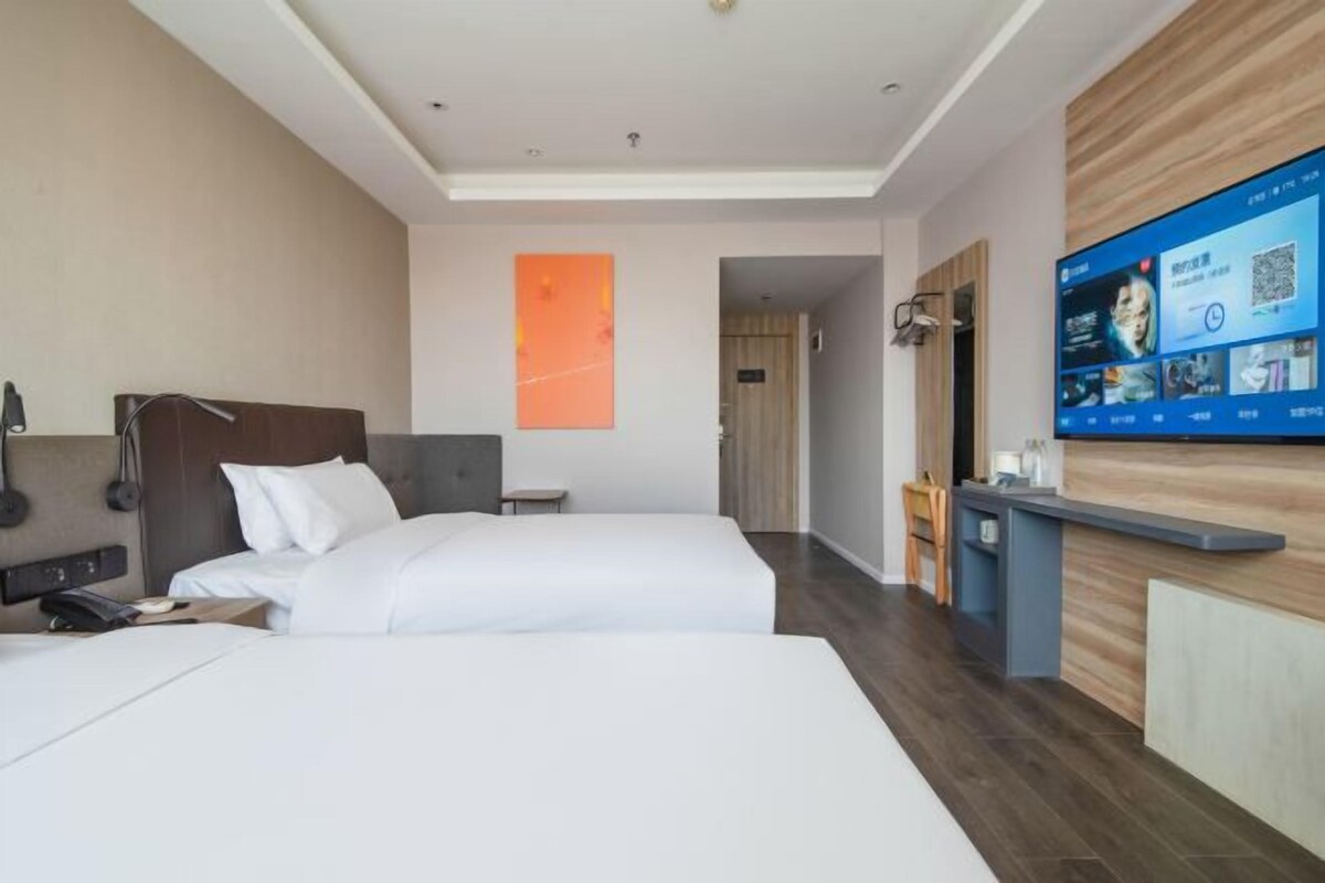 Una camera d'albergo con due letti, una scrivania e un ampio schermo digitale con informazioni.