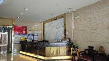 Ein Hotel-Empfangsbereich mit einer Marmor-Rezeption, einem digitalen Bildschirm und einer Sitzecke mit Stühlen.